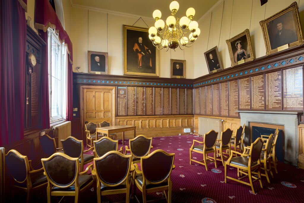 An empty wood-panelled committee room with a long table and chairs arranged for a meeting