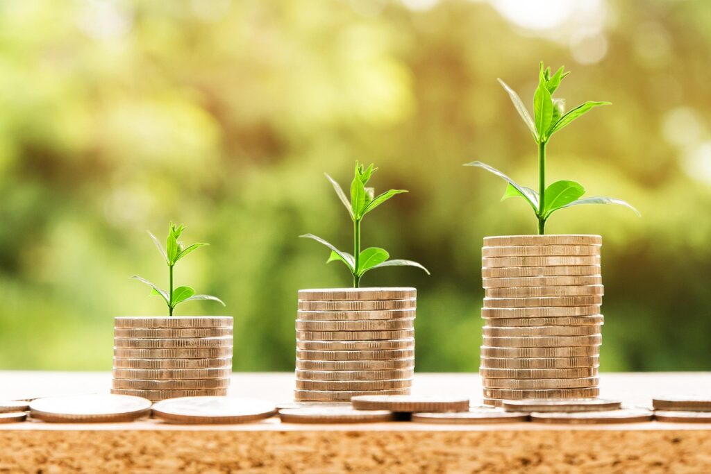 Three ascending stacks of coins with small green plants growing on top, symbolizing money and dividends growing over time