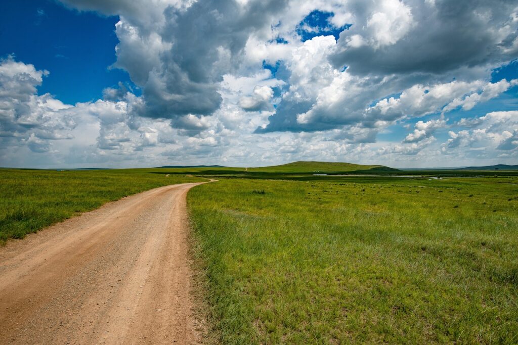 A dirt road winding through a green meadow under a dramatic sky, symbolizing the start of a long journey