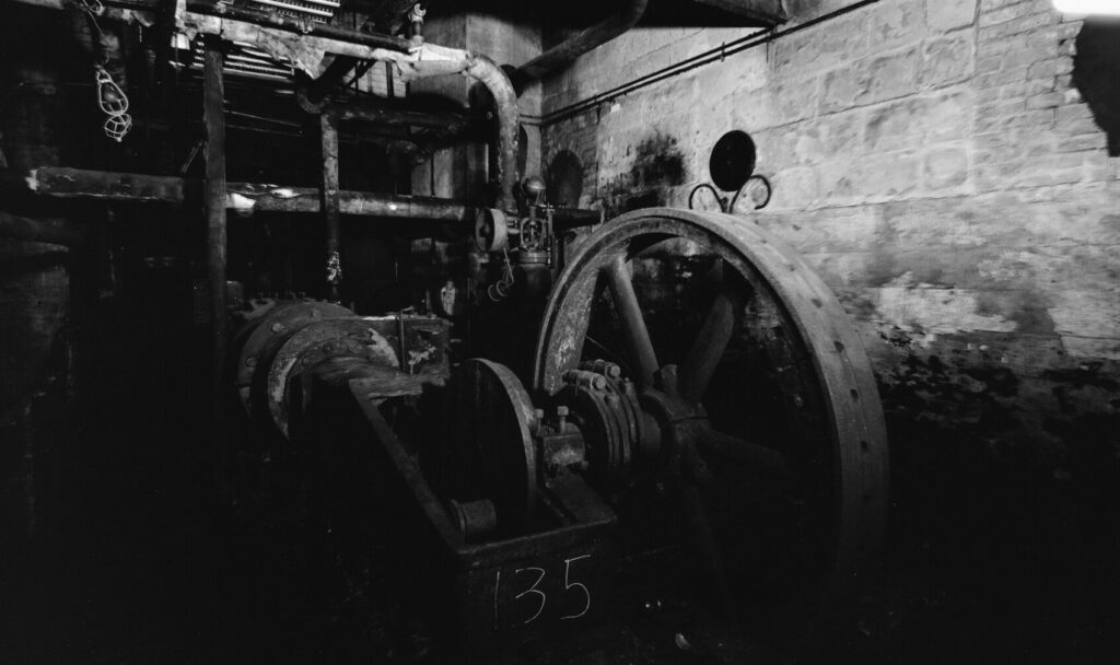 A large steam-driven air compressor in an old power plant, its flywheel and connecting rod linking one moving part to the next